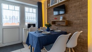 A dining area with a table set for four, a TV mounted on the wall, and a window with curtains. - Gemutliche Ferienwohnung in Tating (Tating)