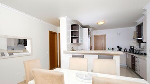 A modern kitchen with white cabinets, a built-in island, and a dining area with a white table and chairs. - Apartment, Lagos - Formerly TUI Ferienhaus (Lagos)