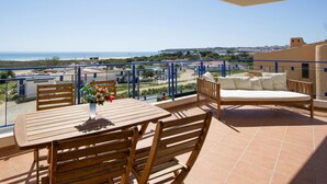 A balcony with a wooden table and chairs, a sofa, and a view of the beach and cityscape. - Apartment, Lagos - Formerly TUI Ferienhaus (Lagos)