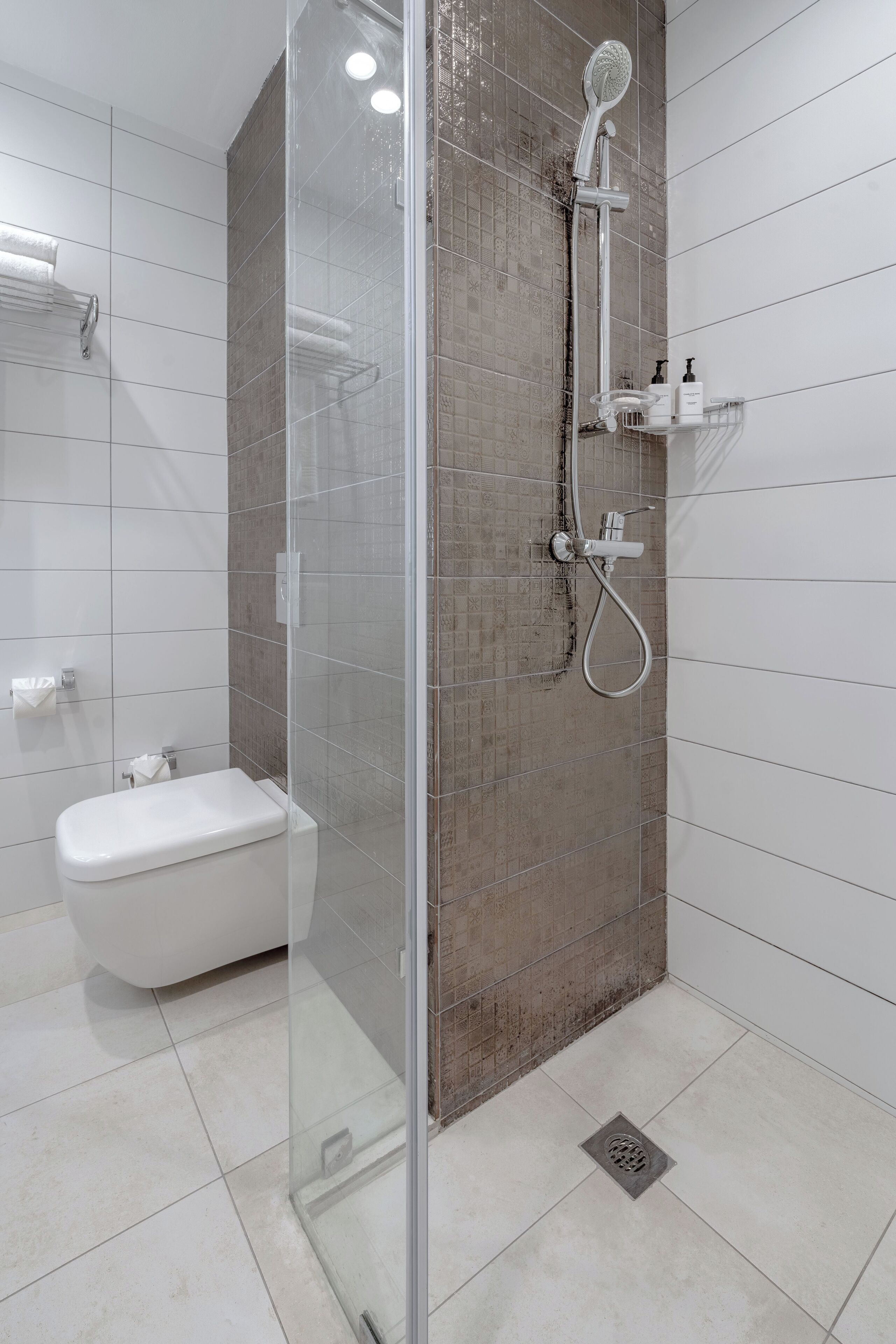 Ein modernes Badezimmer mit einer Glaskabinentrennung für die Dusche, einer weißen Toilette und einem gefliesten Boden.