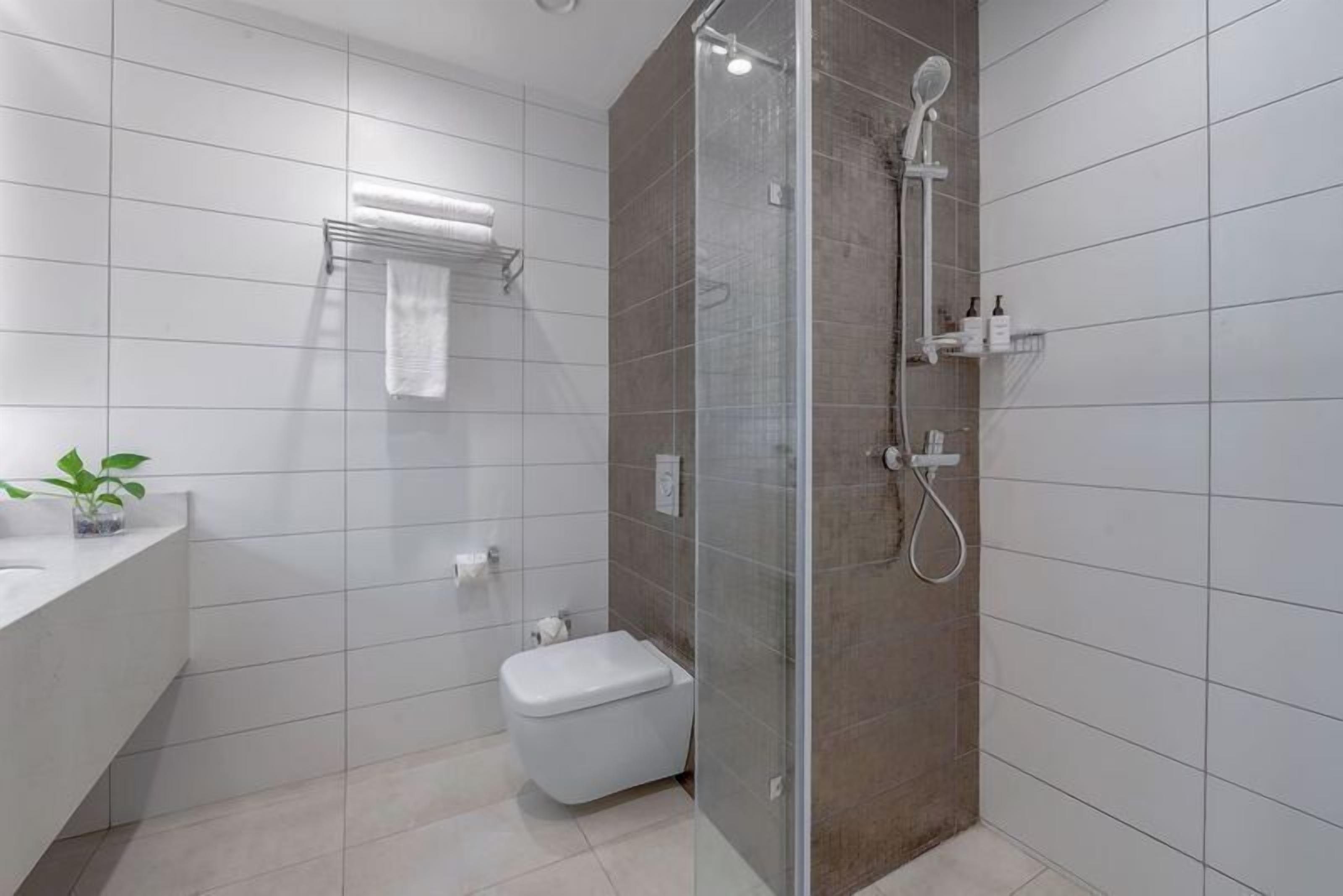 A modern bathroom with a glass-enclosed shower, a toilet, and a sink with a plant.