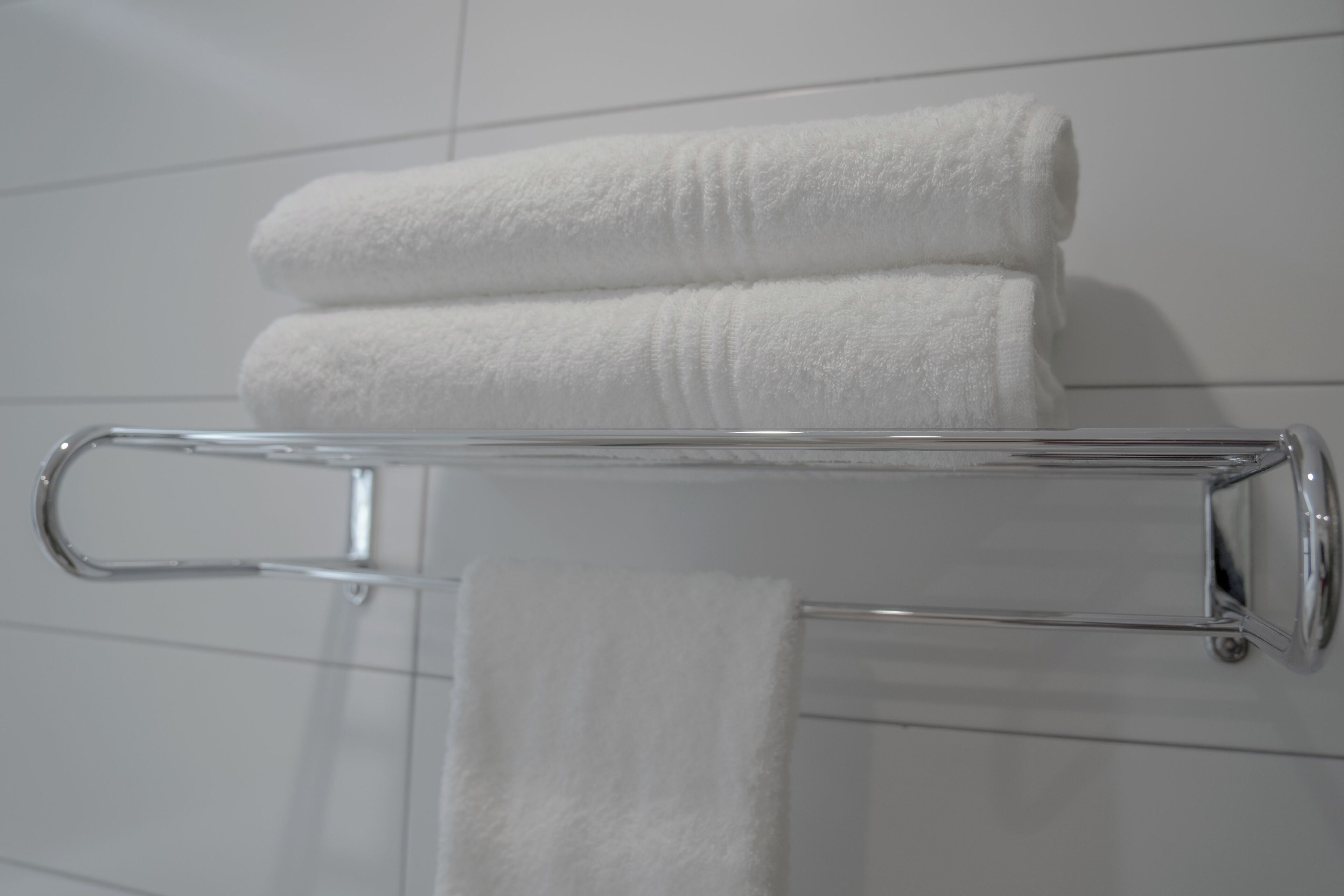 A bathroom with a towel rack holding two neatly folded white towels.