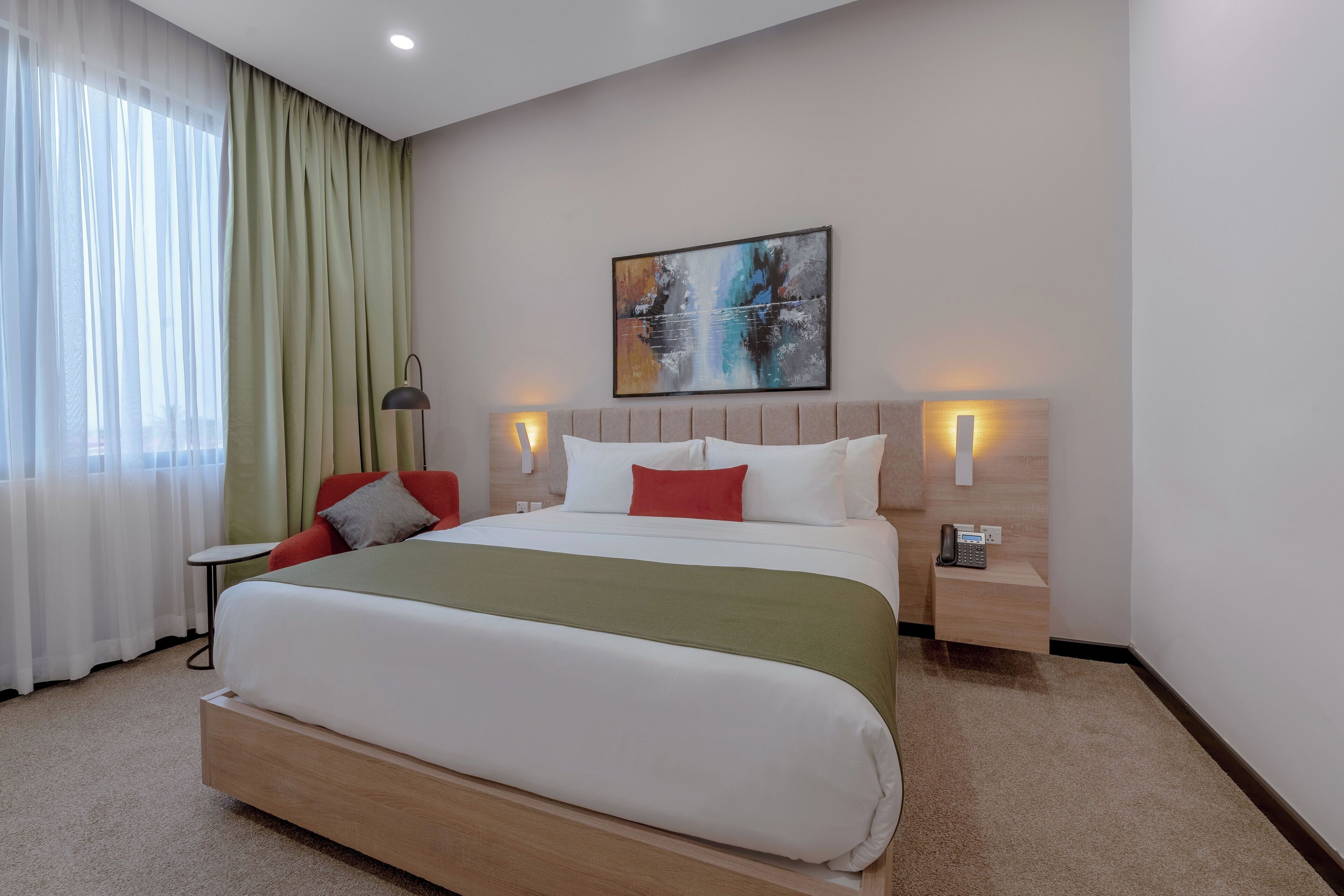 Una habitación de hotel moderna con una cama grande, una mesita de noche con teléfono y un cuadro en la pared.