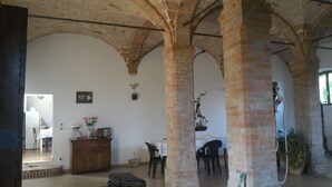 An interior with exposed brick arches, a wooden cabinet, a table with chairs, and a hanging plant. - Agriturismo Cordiglianello  (Perugia)