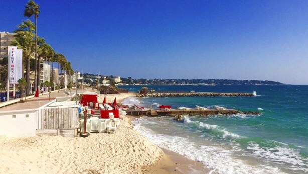 A beach with a wooden pier, palm trees, and a row of beach chairs and umbrellas. - Apartment in Pegomas With Private Pool (Pegomas)