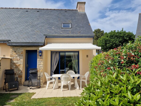 A house with a stone exterior, a tiled patio, a barbecue area, and a covered outdoor seating area with white chairs and a table. - Holiday Home in Erquy Near Sandy Beaches (Erquy)
