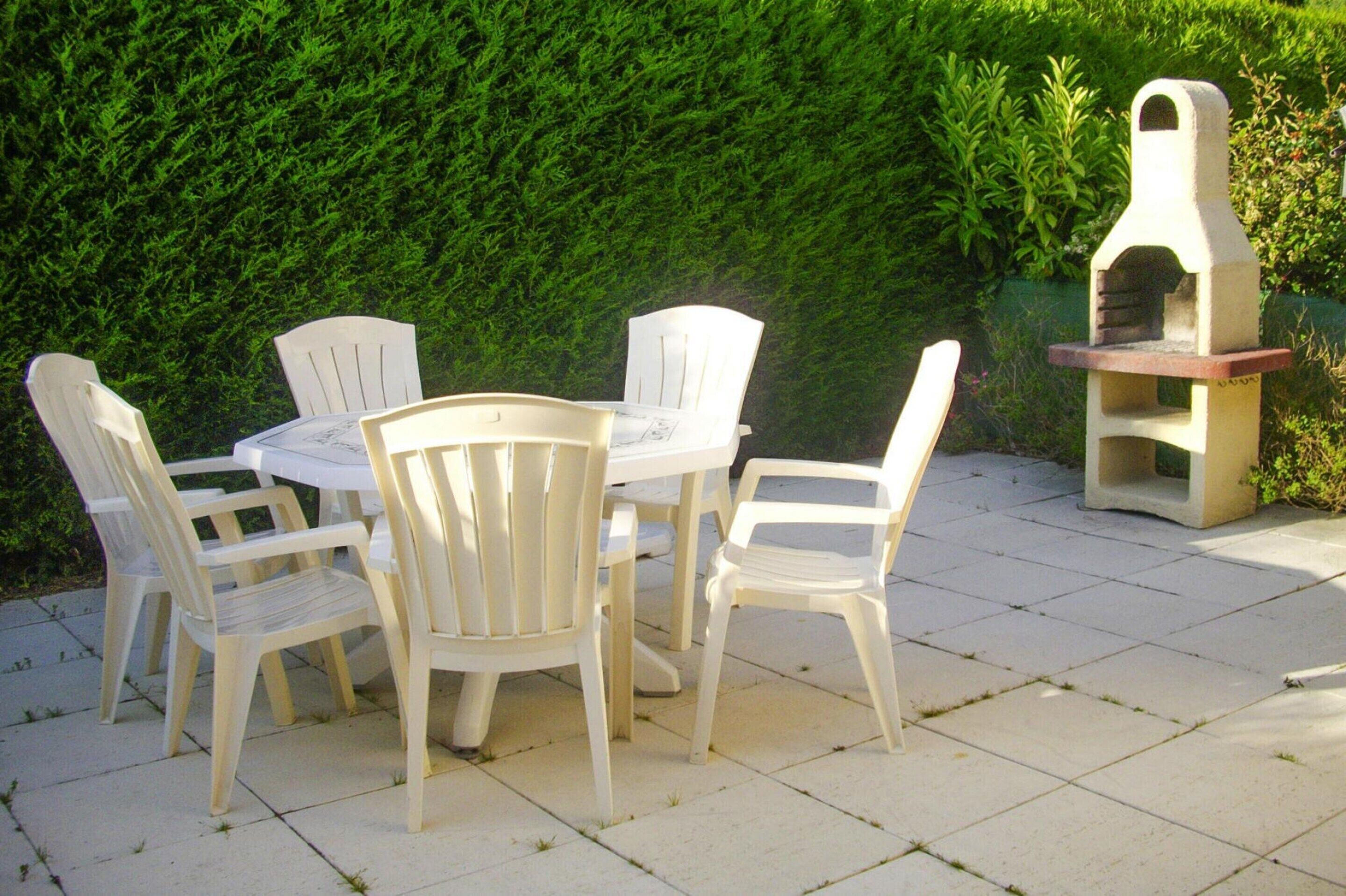 A patio with a table and chairs, a small brick oven, and a hedge in the background.