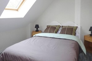 A bedroom with a bed, two nightstands, a window, and a sloped ceiling. - Holiday Home in Erquy Near Sandy Beaches (Erquy)