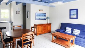 A dining area with a wooden table and chairs, a blue sofa, and a wooden cabinet. - Holiday Home in Erquy Near Sandy Beaches (Erquy)
