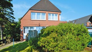 A two-story brick house with a gabled roof, a visible number '6' on the side, and a well-maintained front yard with a large bush. - Ferienwohnung in Westerland-ex TUI (Sylt)