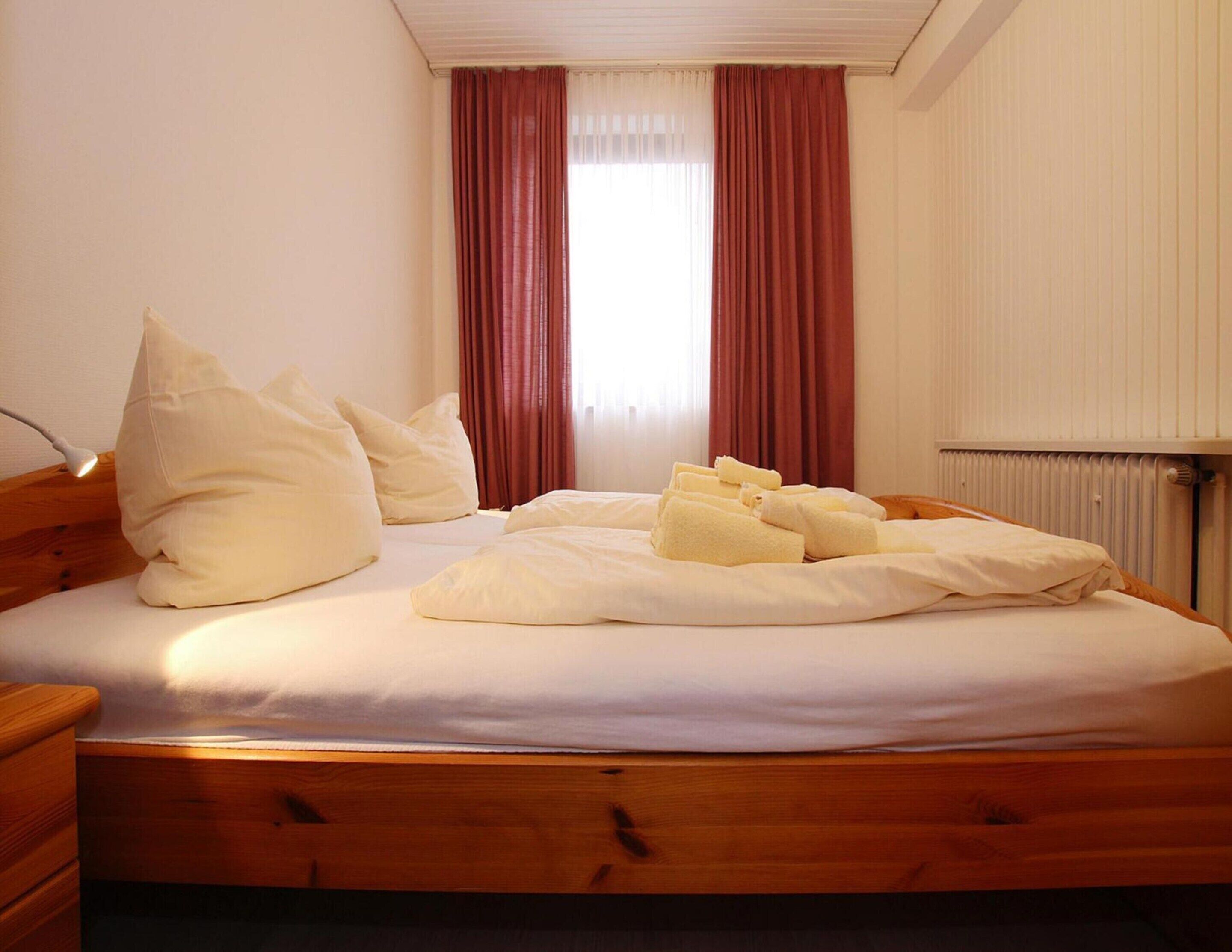 Una cama bien hecha con almohadas y toallas, un cabecero de madera y una ventana con cortinas.