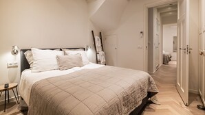 A bedroom with a bed, bedside table, lamp, and a door leading to another room. - Luxury Apartment with spacious living room (Amsterdam)