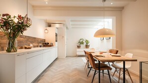 A modern kitchen with white cabinetry, a wooden herringbone floor, and a dining area with a wooden table and chairs.