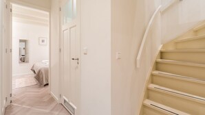A hallway with a staircase, a bed, and a door.