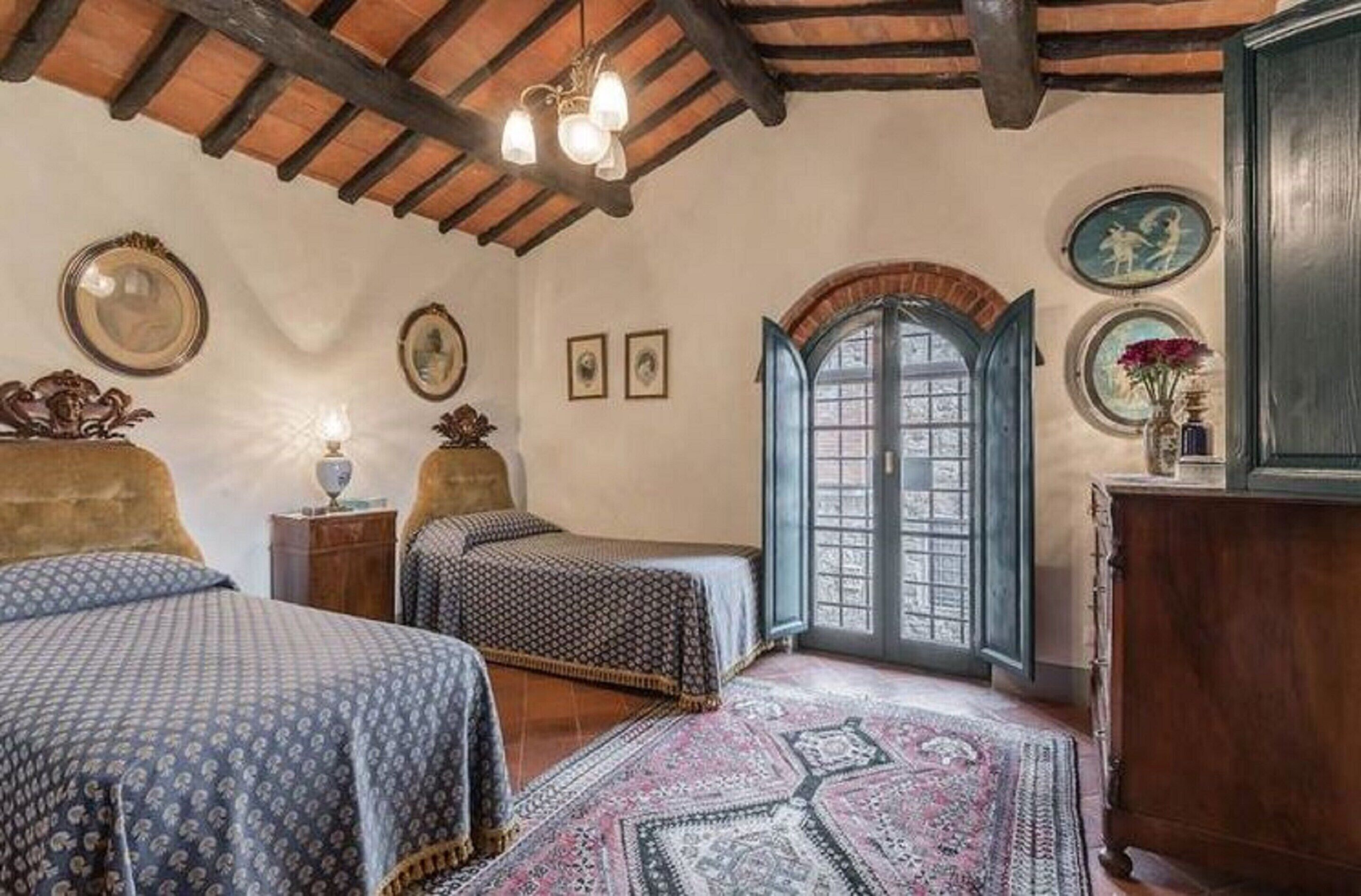 A bedroom with two beds, a wooden ceiling, a large window, and a traditional door.