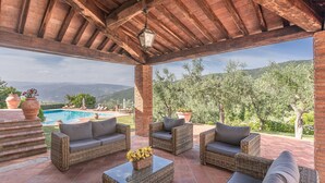 Una terrazza esterna con mobili in vimini, una piscina e vista sulle montagne.