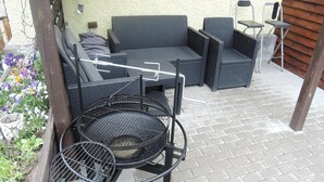 Un patio al aire libre con una parrilla redonda, mobiliario de mimbre y piso de ladrillo.