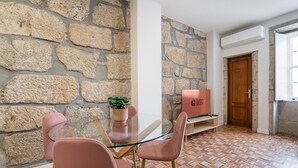 Una habitación moderna con pared de piedra, una mesa de vidrio, sillas rosas, una puerta de madera y un televisor que dice "GUEST READY".