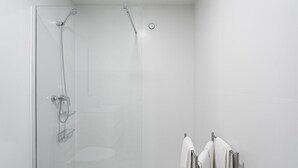 Un baño moderno con cabina de ducha de vidrio, inodoro y toallero con toallas.