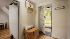 Ein Zimmer mit Holzboden, einem Korbwäschekorb, einer zur Außenseite führenden Tür und einem an der Wand befestigten Regal mit Bildern.