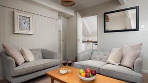 A living room with two grey sofas, a wooden coffee table with a fruit bowl, and a wall clock. - One Bedroom Cottage in the heart of Beadnell (Beadnell)