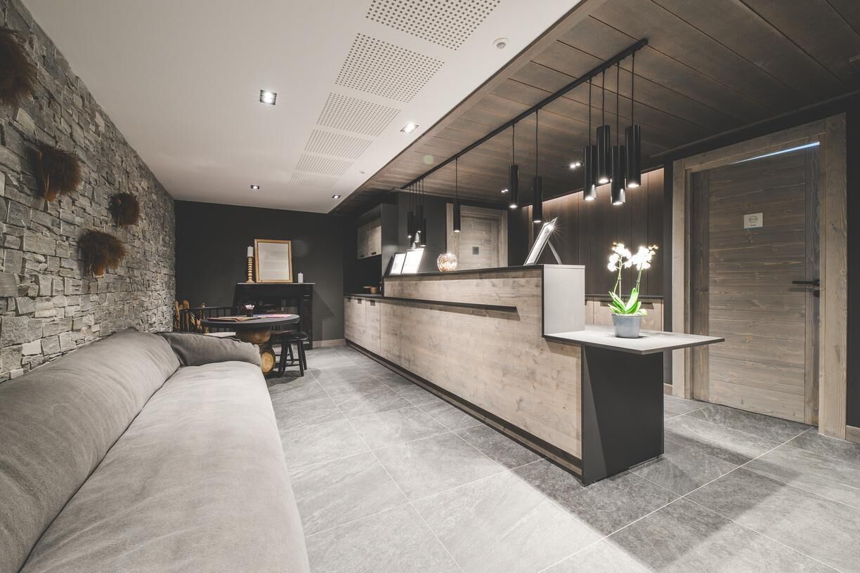 A modern interior with a stone wall, a reception desk, a sofa, and a dining area. - Wifi, 100m from ski slopes, sauna, hammam, balcony, parking, ski locker, 87m², Peisey-Vallandry (Mâcot-la-Plagne)