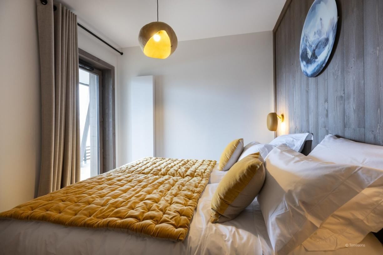 A bedroom with a large bed, a hanging light fixture, a wall-mounted light, and a window with curtains.