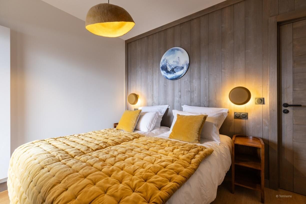 Een slaapkamer met een groot bed, een houten hoofdeinde, twee nachtkastjes en een wandlamp.