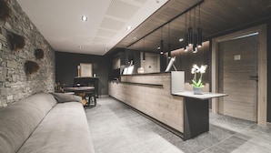 A modern interior with a stone wall, a reception desk, a sofa, and a dining area. - Wifi, 100m from ski slopes, sauna, hammam, terrace, parking, ski locker, 103m², Peisey-Vallandry (Mâcot-la-Plagne)