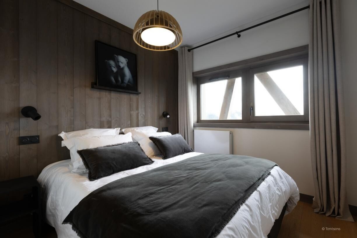 A bedroom with a large bed, a wooden headboard, a wall-mounted TV, and a window with curtains.
