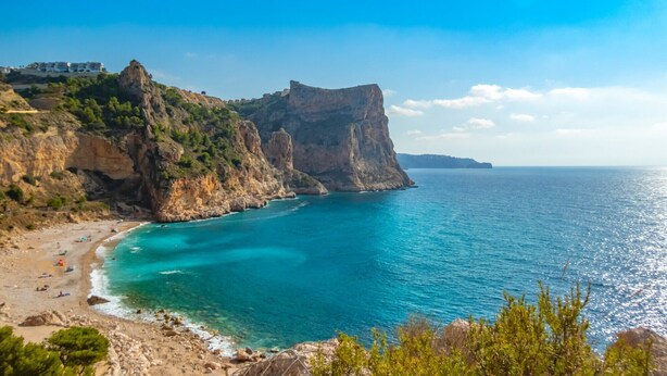 Un paisaje costero con un acantilado rocoso, una playa y un mar azul y transparente.