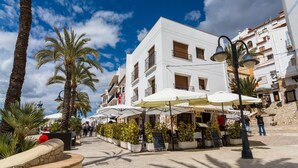 Un edificio blanco con balcones, mobiliario exterior con sombrillas y palmeras.