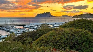 Un puerto deportivo con barcos amarrados, rodeado de vegetación y montañas al atardecer.
