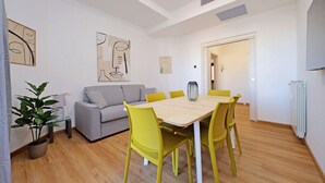 A modern living room with a dining table, yellow chairs, a grey sofa, and abstract wall art.
