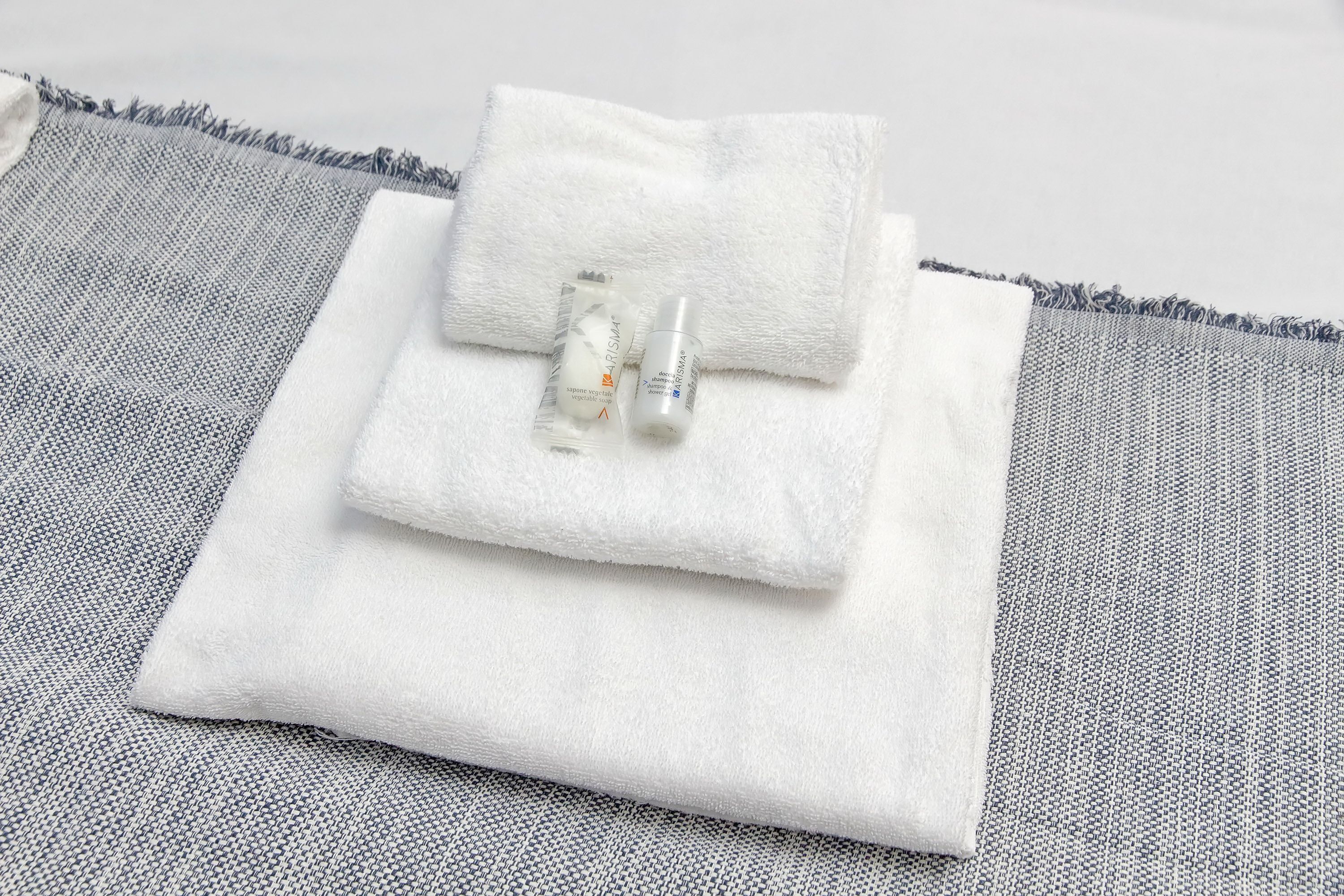 Une serviette blanche et deux flacons de produits de toilette sont posés sur un tapis tissé gris.