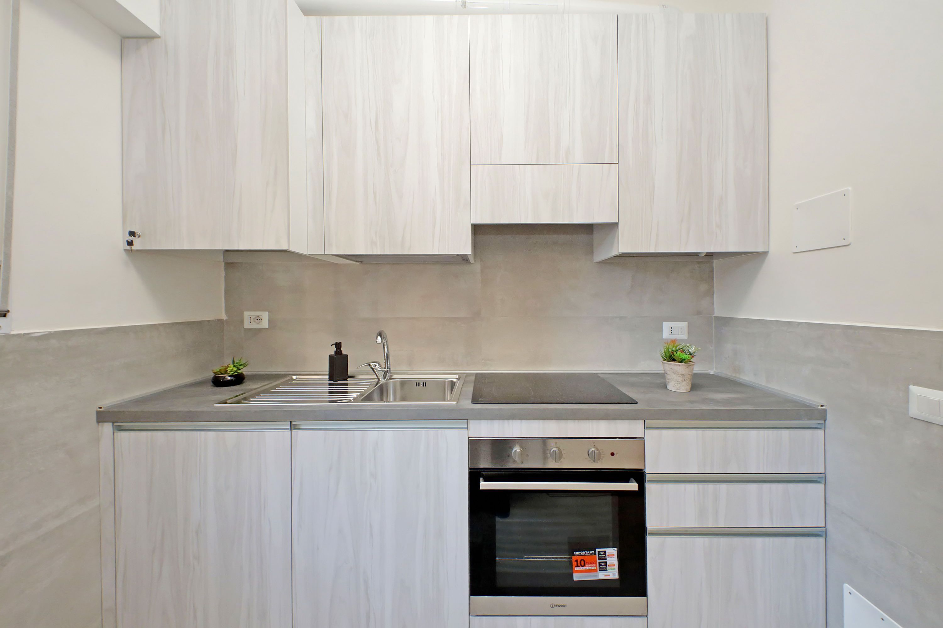 A modern kitchen with light wood cabinets, a stainless steel sink, and a built-in oven.