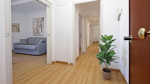 A hallway with a wooden floor, a grey sofa, and a potted plant.