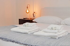 Ein ordentlich bezogenes Bett mit weißen Kissen und gefalteten Handtüchern, eine Nachttischlampe und eine Steckdose auf dem Nachttisch.