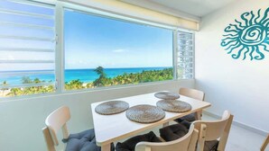 A dining area with a table and chairs, a view of the ocean, and a decorative wall piece.
