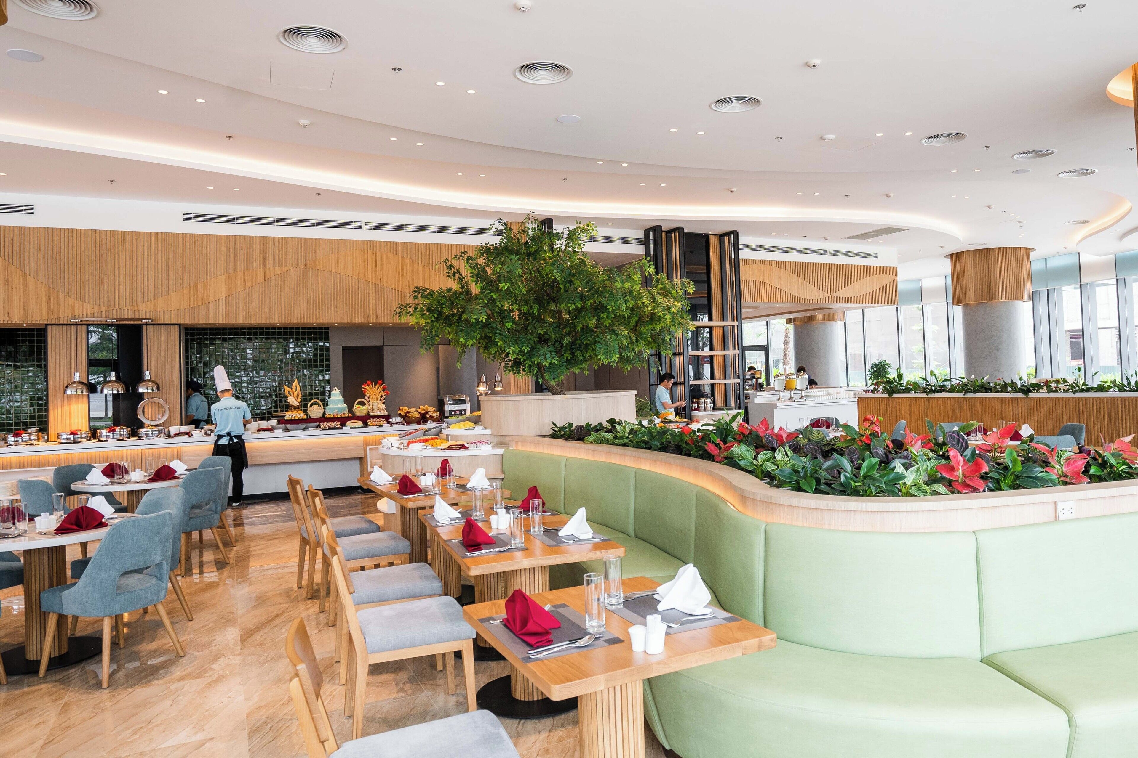 A modern restaurant with a central seating area, a buffet, and a large tree.