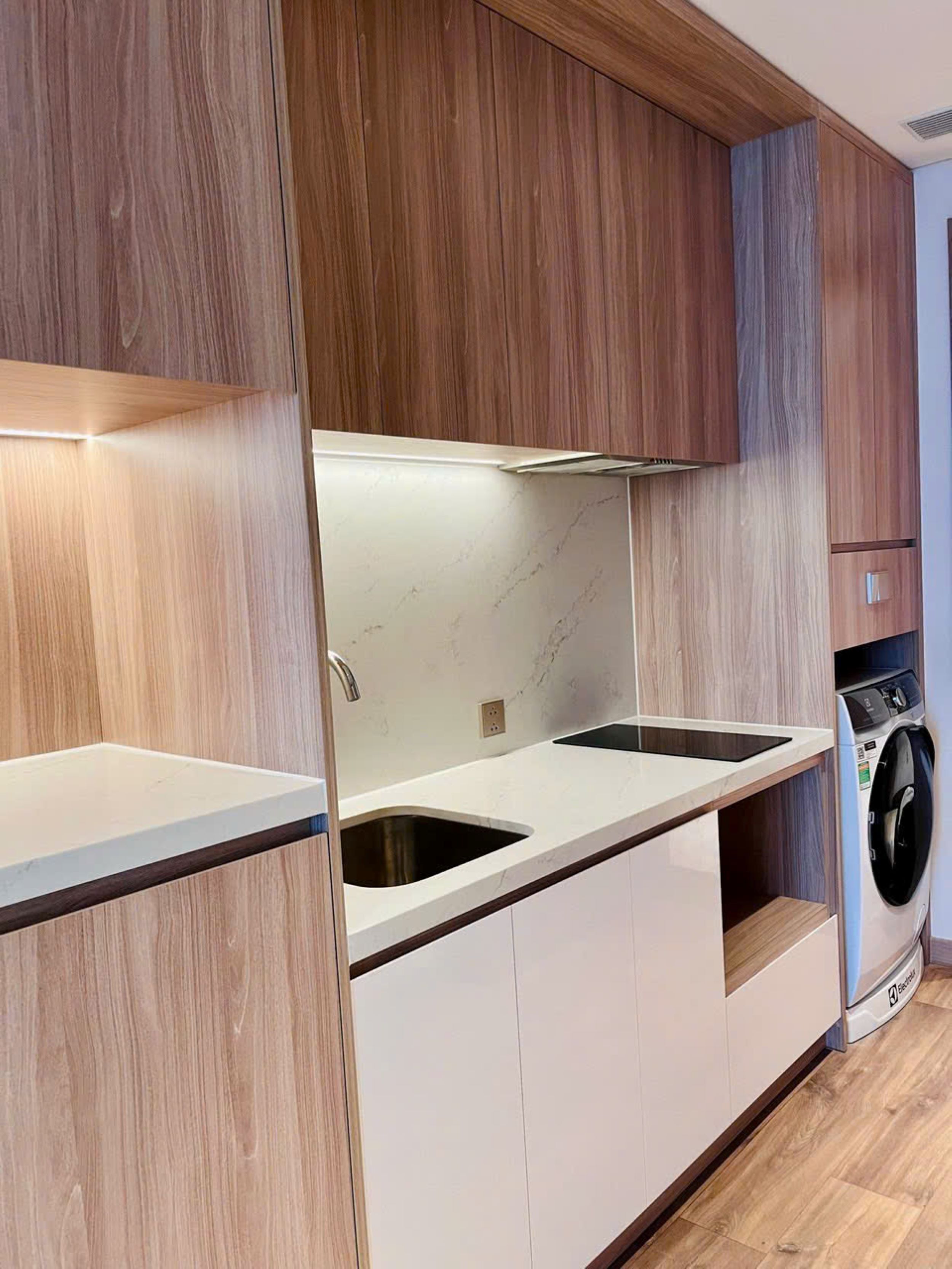 A modern kitchen with wooden cabinetry, white countertops, and a built-in washing machine.