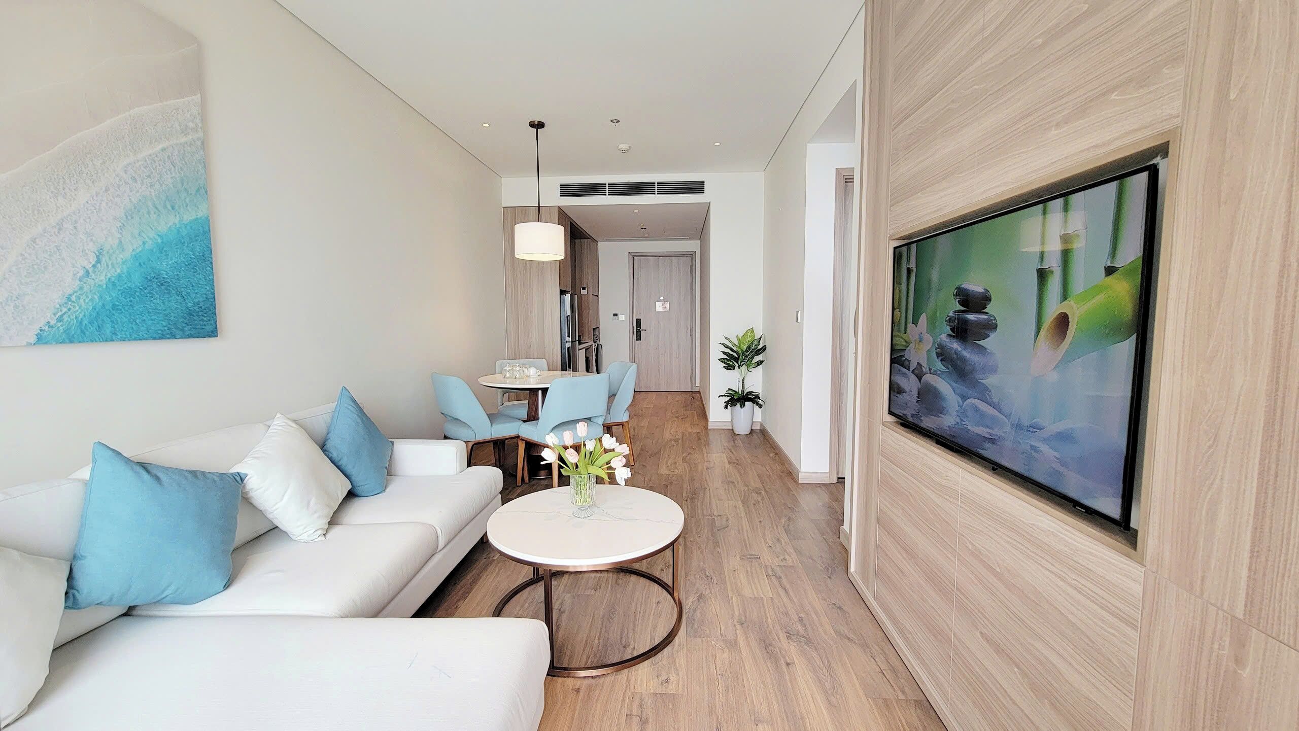 Un salon moderne avec un canapé blanc, une table basse ronde et un téléviseur à écran plat fixé au mur.