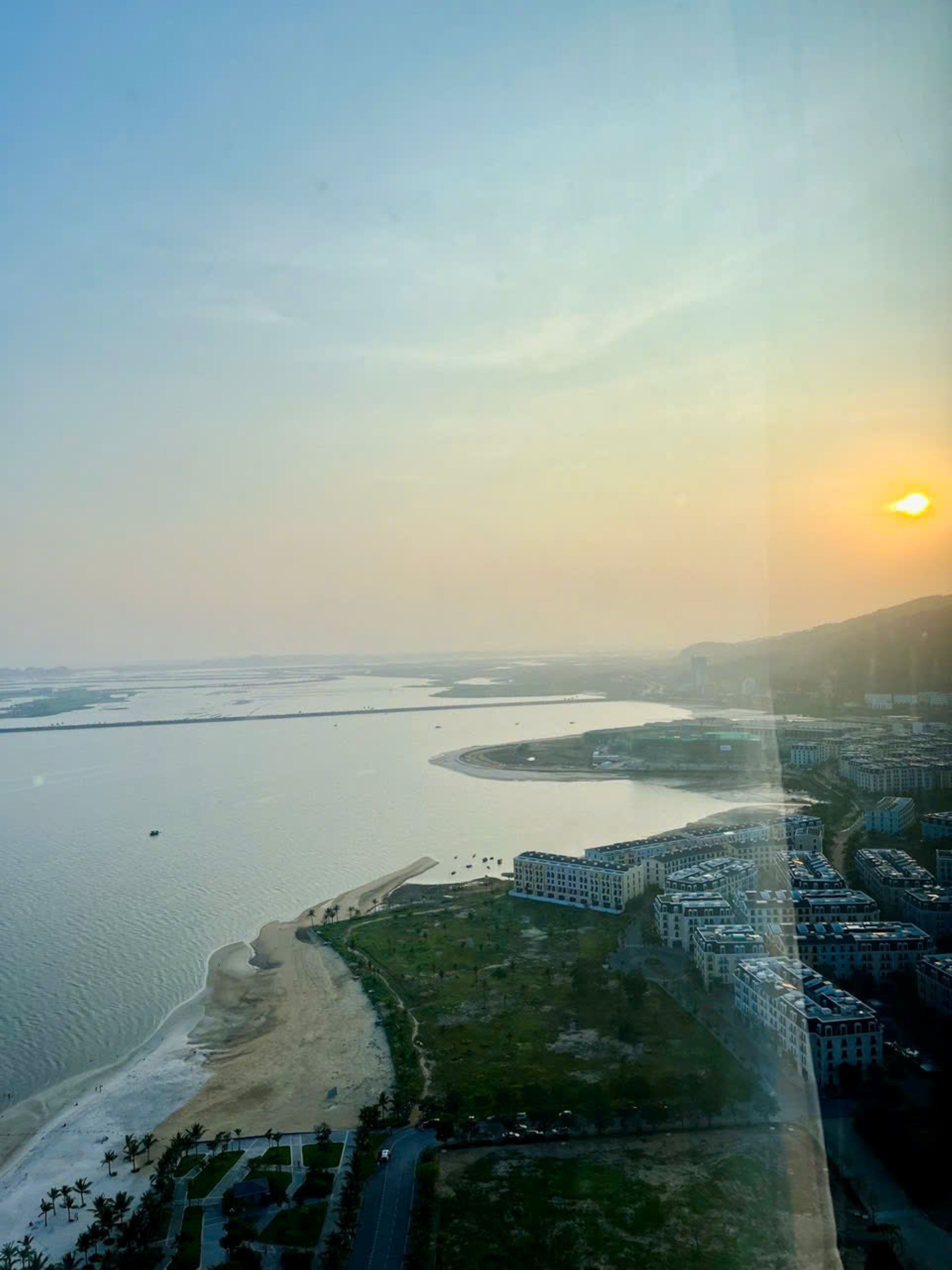 An aerial view of a coastal area with a beach, a river, and a cluster of buildings.