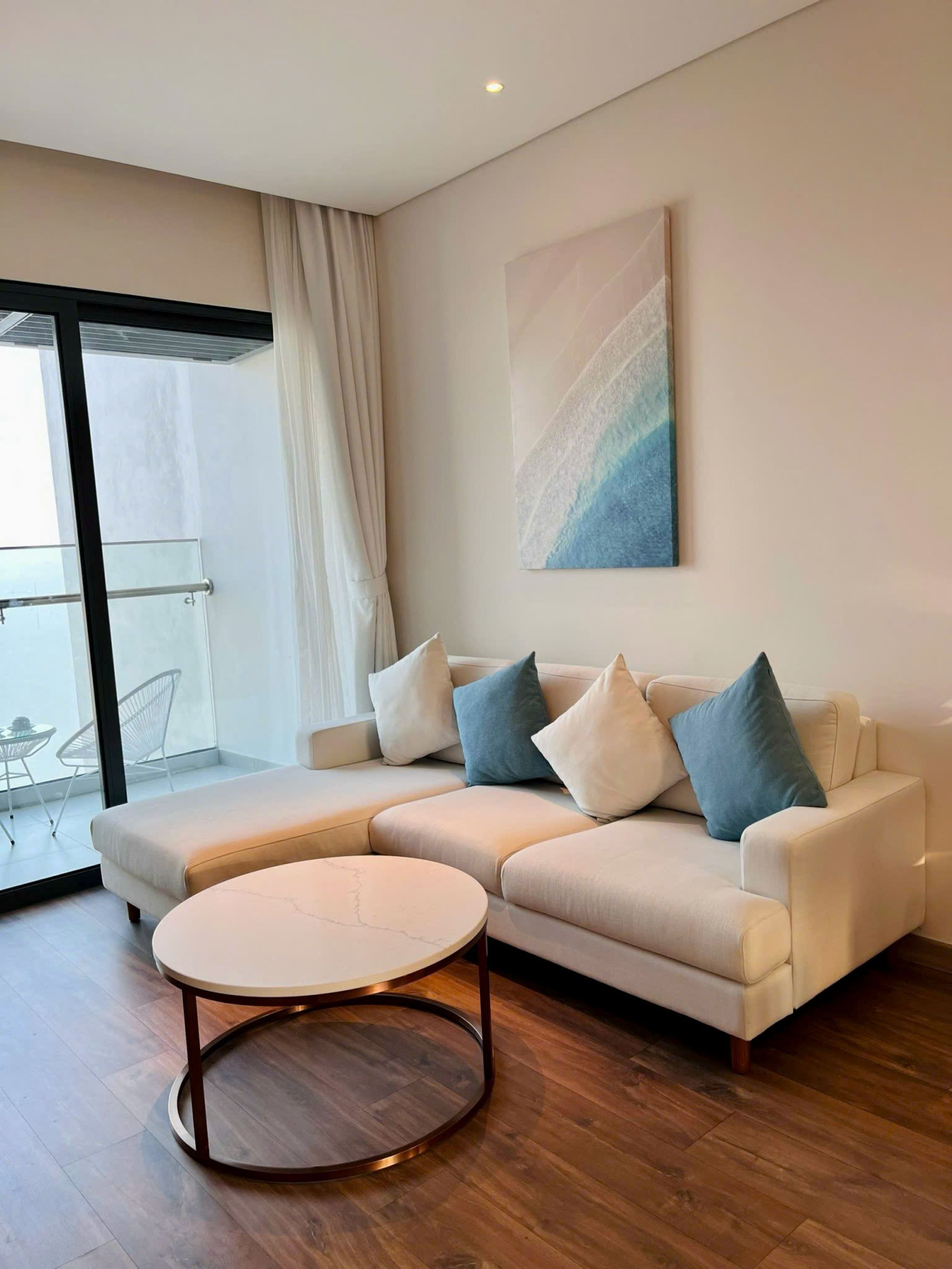 A modern living room with a beige sectional sofa, a round coffee table, and a large abstract painting on the wall.