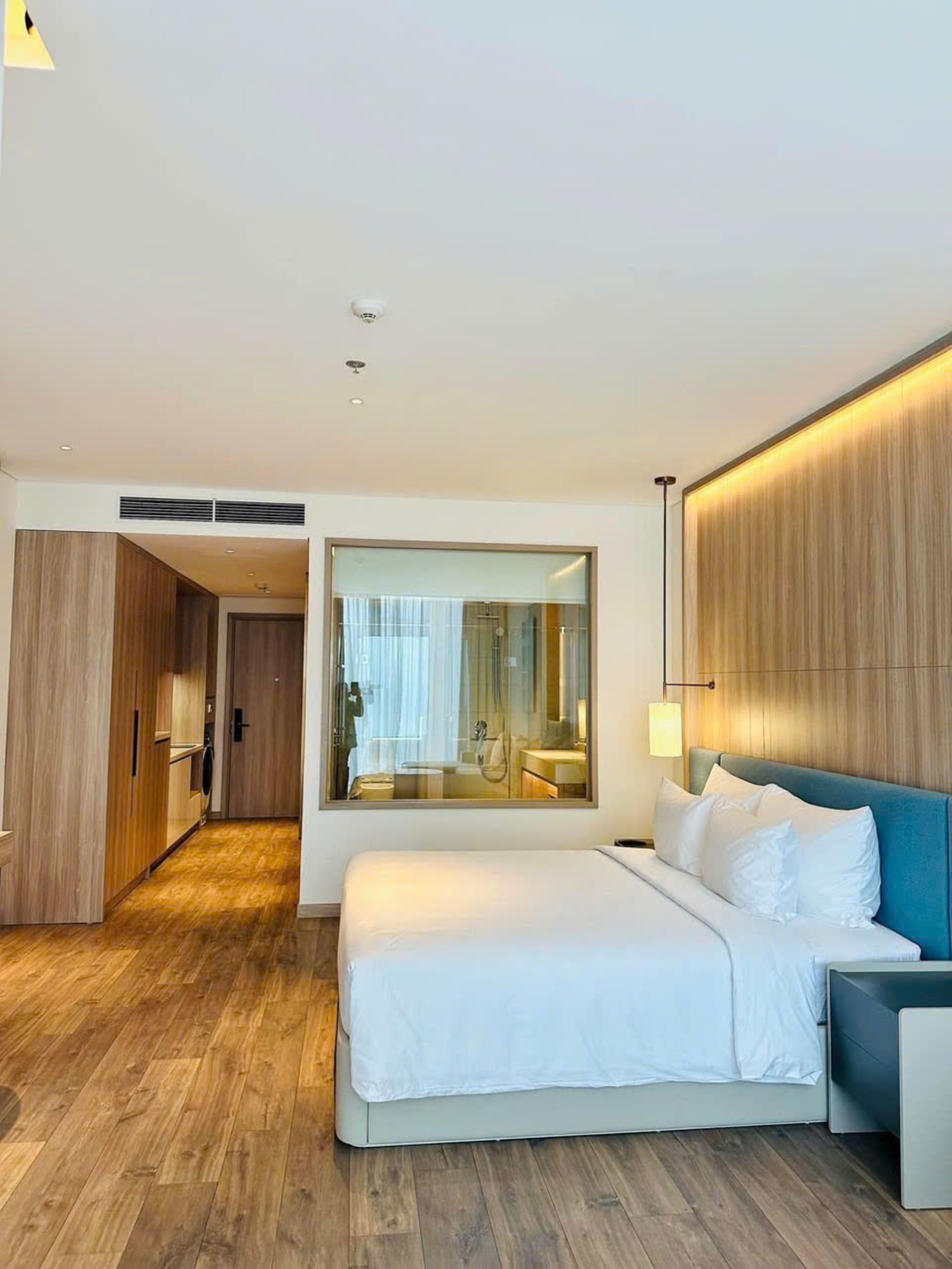 Habitación de hotel moderna con una cama grande, un armario de madera, un espejo y vistas al baño.