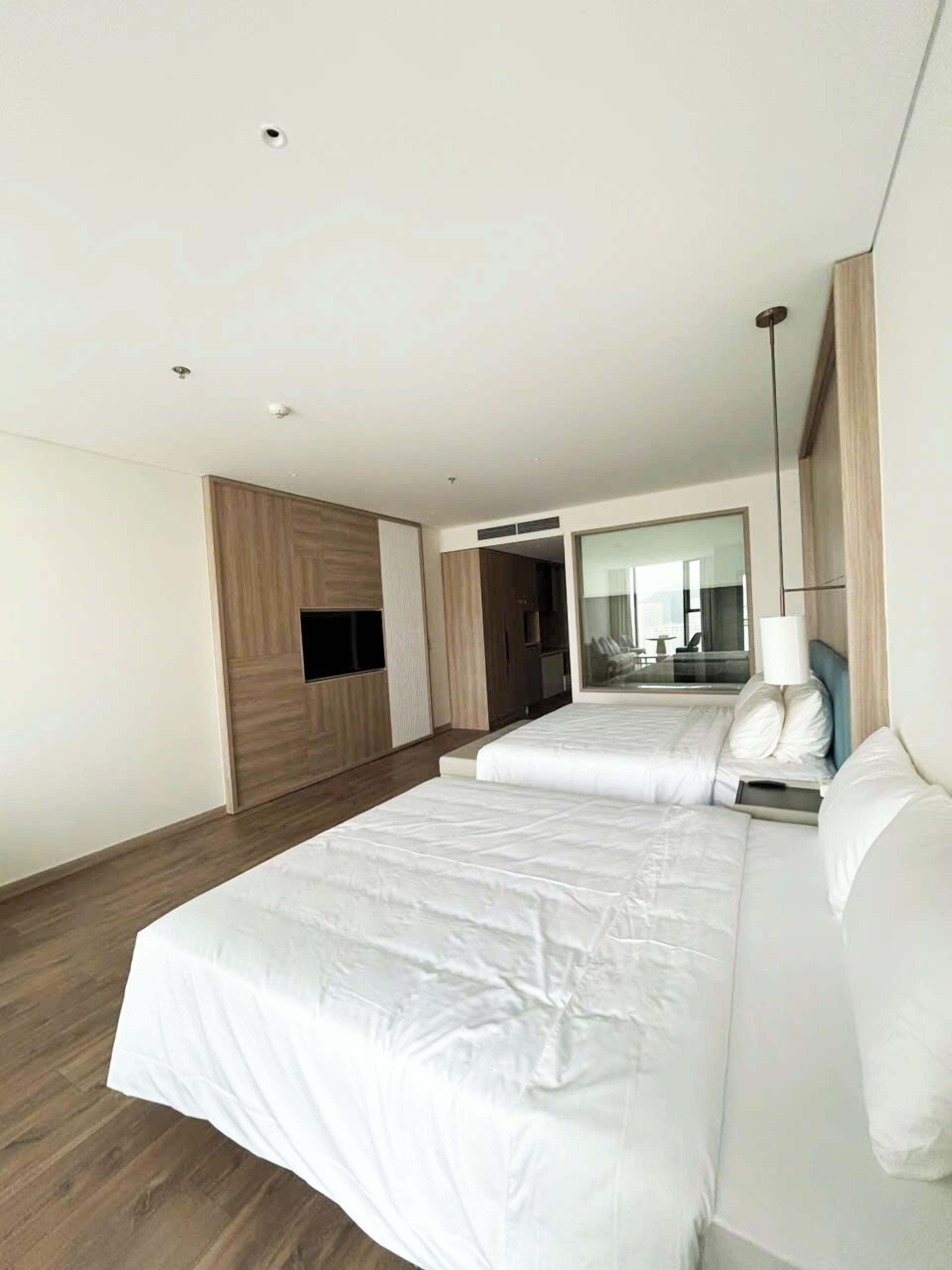 Een moderne hotelkamer met een groot bed, een flatscreen televisie aan de muur en een grote spiegel die de kamer weerspiegelt.