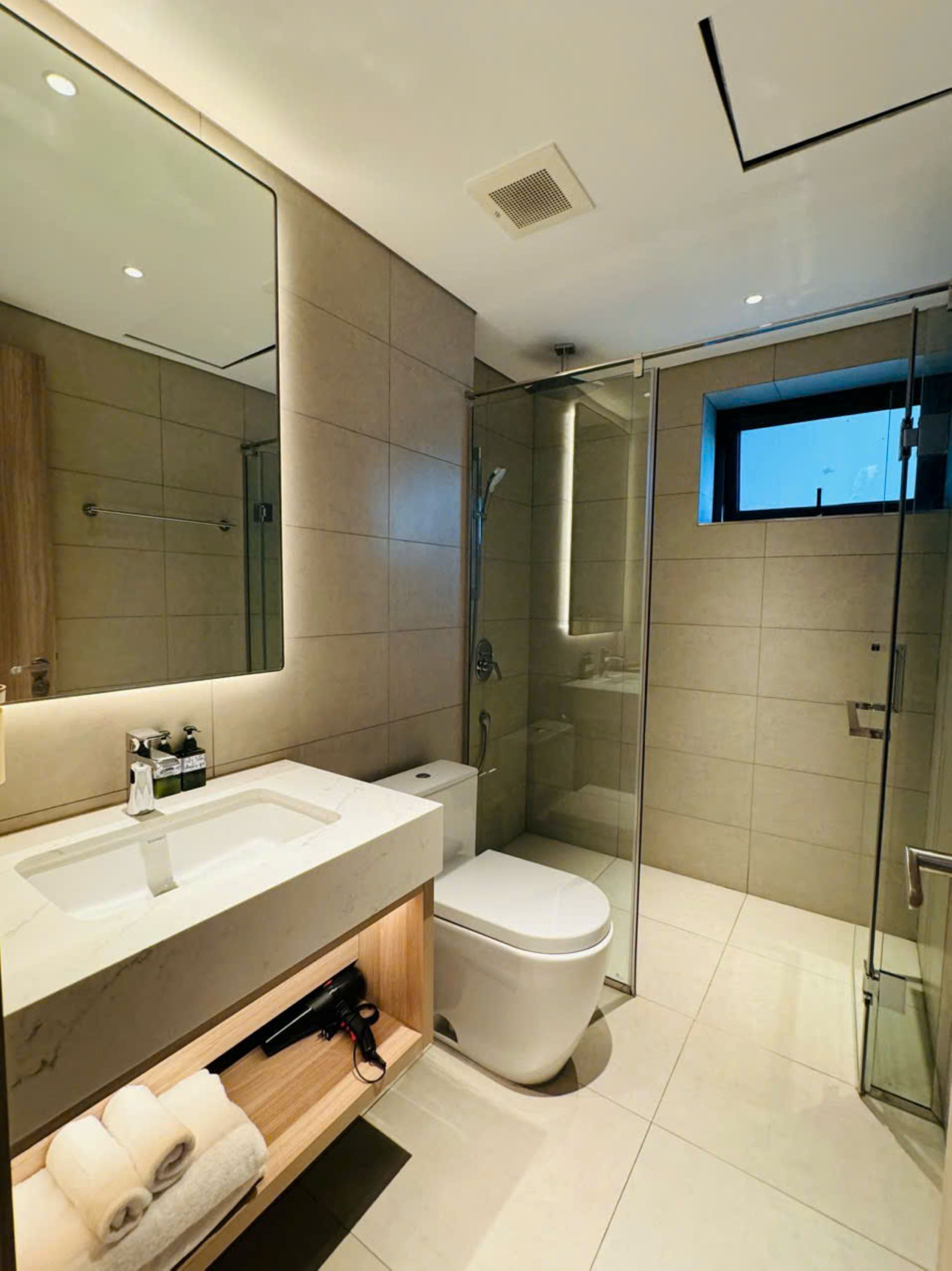 A modern bathroom with a large mirror, a glass shower enclosure, a toilet, and a vanity with a sink and towel rack.