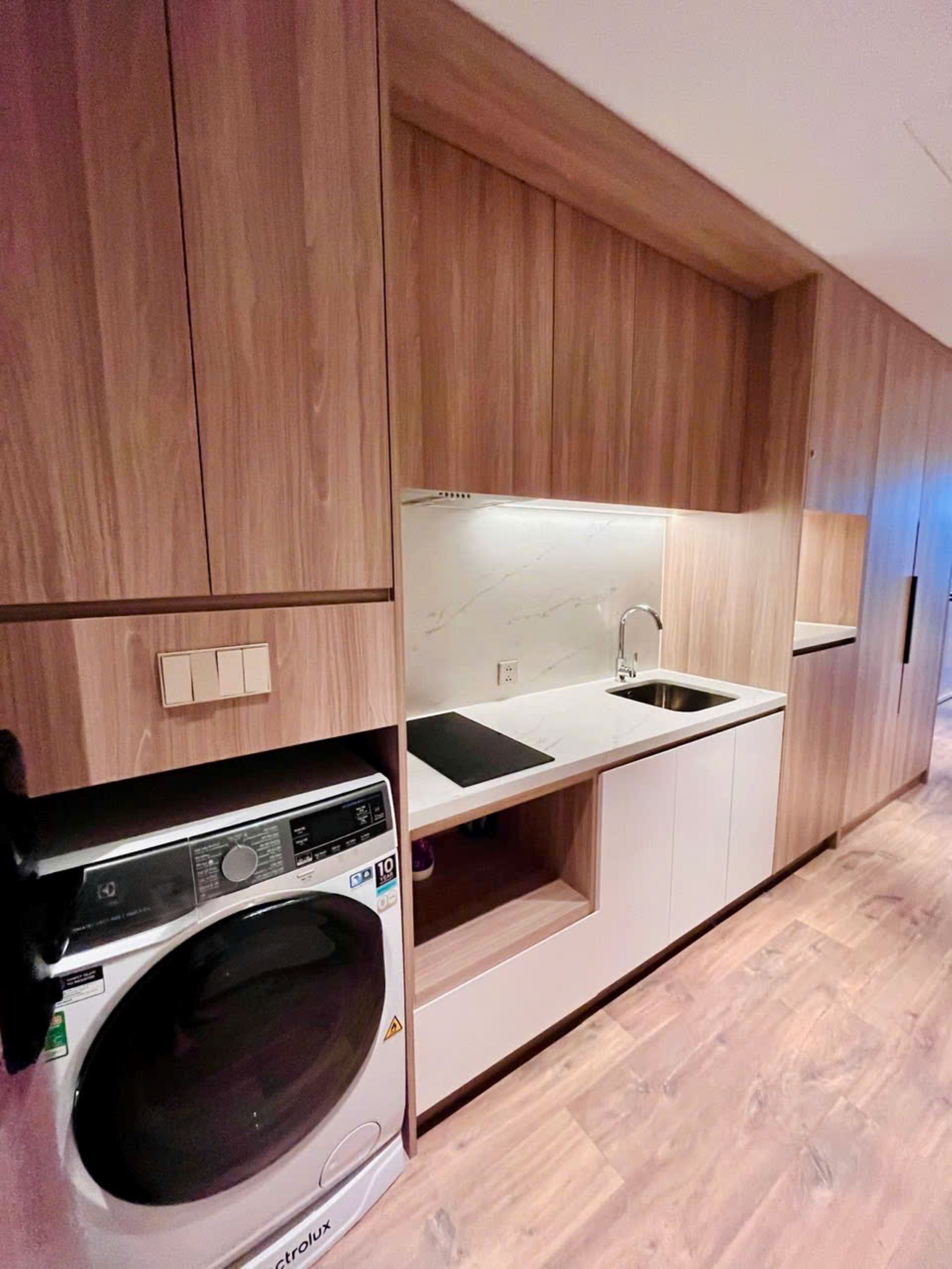Une cuisine compacte avec des meubles en bois, un lave-linge encastré et un petit plan de travail avec un évier.