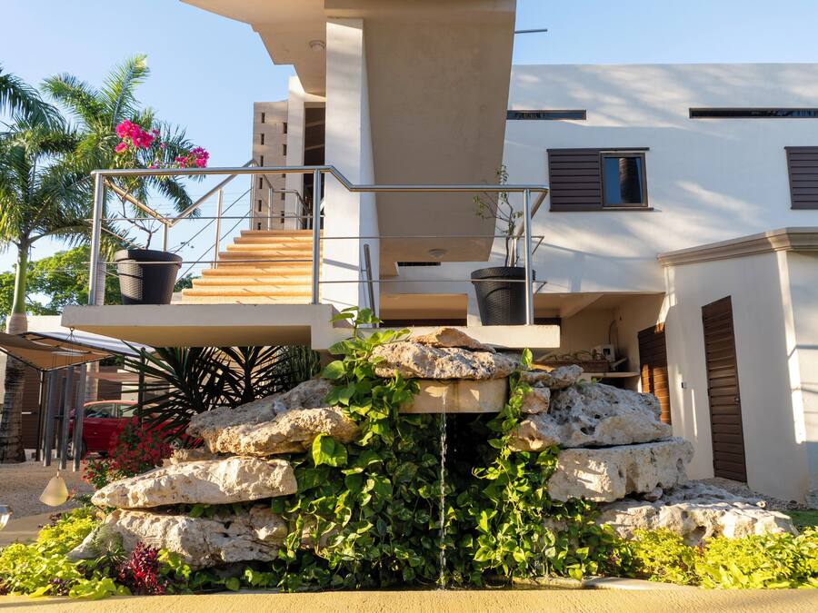 A modern building with a stone water feature, a staircase, and a balcony with potted plants.