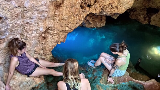 Three individuals sitting on rocky formations near a clear blue water body within a cave. - Azcapri Villa-Boutique & Spa (Cancun)
